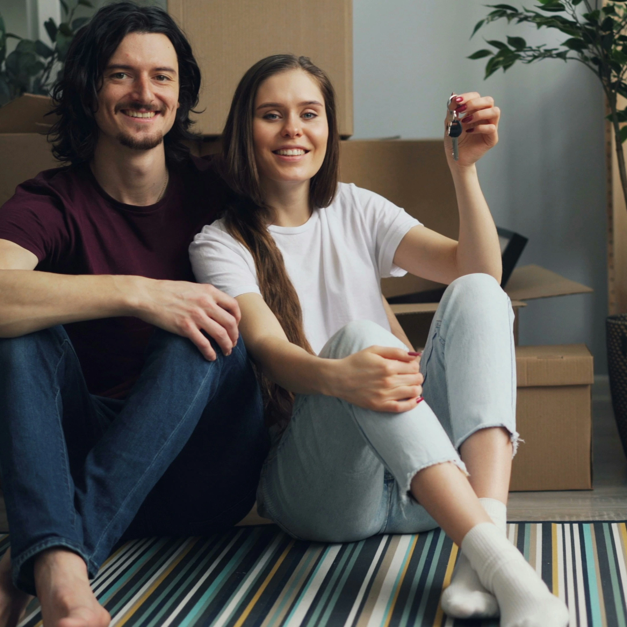 A couple holding their new home keys, surrounded by moving boxes